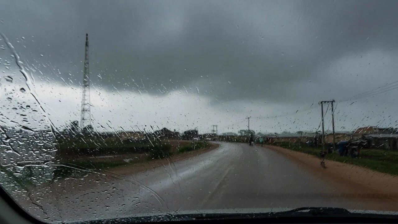 A wet road in Jos seen through a rain-streaked windscreen, under heavy grey cloud.